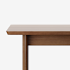 A close-up of a wooden table with a smooth, rectangular top and a visible leg, set against a plain white background.