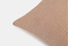 Close-up of a light brown or tan textured pillow with a subtle grid pattern, shown against a plain white background. Only the top left corner of the pillow is visible.