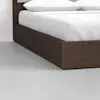Close-up of the corner of a dark wooden bed frame with white bedding and pillows, placed on a smooth, light gray floor in a minimalistic room.