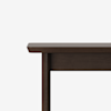 Close-up of the top corner of a dark brown wooden table against a plain white background, showing the edge and part of a leg.