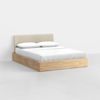 A modern bed with a light wood frame, beige upholstered headboard, and white bedding with two pillows, set in a minimalist room with a light gray floor and white walls.