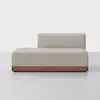 A modern, minimalist beige chaise lounge with a low, rectangular wooden base and an off-center backrest, set against a plain white background.