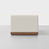 A modern, rectangular ottoman with cream-colored upholstery and a wooden base, photographed against a plain, light gray background.