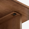 Close-up view of a wooden table or desk corner, showing a dark circular screw or fastener securing the top to the supporting leg, with a smooth, natural wood grain finish.