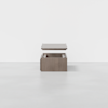 A brown wooden box sits on a light gray floor with its lid lifted and hovering above the box, against a plain white background.