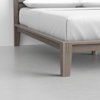 Close-up of a modern wooden bed frame with light-colored wood and clean lines, supporting a neatly made bed with white sheets and pillows on a smooth, light gray floor.