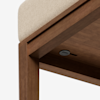 Close-up of a wooden bench or table with a beige cushioned seat, showing the corner detail and part of the underside, including a small round black button or plug.