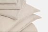 A neatly folded stack of beige bed linens, including pillowcases and sheets, arranged on a white background.