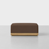 A square, brown ottoman with a textured fabric top and a light wooden base, placed on a smooth, light-colored floor against a plain white background.