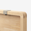 Close-up of the corner of a light wood cutting board with rounded edges, featuring a small, rectangular gray attachment on the top edge, against a plain white background.