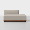 A modern, armless beige chaise lounge with a low backrest and a wooden base, placed on a light gray floor against a plain white background.