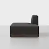 A modern, dark gray armless sofa with a low wooden base, viewed from the side against a plain white background.