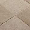 Close-up of a textured carpet with a geometric pattern formed by intersecting seams, creating four square sections in slightly different shades of beige. The surface shows a mix of looped and cut pile textures.