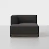 A modern, dark gray upholstered sectional sofa with a low back and armrest on the left side, set on a wooden base, sits on a light gray floor against a plain white background.