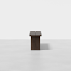 A minimalistic, rectangular wooden bench with a dark finish is centered on a plain, light gray background. The photo shows a frontal view, highlighting the bench’s simple and modern design.