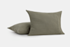 Two olive green square pillows with soft linen covers, one resting upright and the other lying flat on a plain white background.