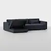 A modern dark gray sectional sofa with a chaise lounge. The chaise has its seat lifted, revealing a hidden storage compartment underneath. The background is plain and light-colored.