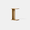 A small, modern side table made of light wood, shaped like the letter C with a flat top and base connected by a vertical panel, placed against a plain white background.