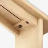 Close-up view of a wooden table joint showing how the tabletop is attached to the leg with black hex bolts and precise craftsmanship, highlighting the clean and modern design.