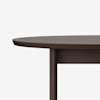 Partial view of a round, dark wooden table against a plain white background; only the tabletop edge and a single vertical leg are visible.