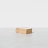 A small, rectangular, light wood storage box with a simple, minimalist design sits on a smooth, light gray surface against a plain white background.
