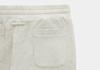 Close-up of the upper section of light beige sweatpants, showing the elastic waistband, stitched seam, and a rectangular back pocket with a ribbed edge on a plain white background.