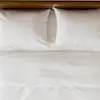 Close-up of a neatly made bed with white sheets, pillows, and a comforter, featuring a gray upholstered headboard and frame on a wooden floor.