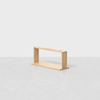 A minimalist wooden rectangular shelf or rack with an open design, placed on a light gray surface against a plain white background.