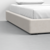 A close-up view of a modern bed with a beige upholstered frame and white bedding, set on a smooth, light gray floor against a plain white wall.