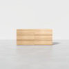 A minimalist, light wood dresser with six drawers is placed against a plain white background and floor.