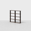 A minimalist, dark wooden bookshelf with three vertical dividers and four horizontal shelves, standing empty on a light, seamless surface against a plain white background.