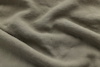 A close-up view of wrinkled, textured beige fabric, showing soft folds and shadows that highlight the material’s natural weave and slightly rough surface.