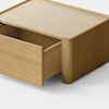 A minimalist wooden box with a single drawer partially open, placed on a light gray surface against a plain white background.
