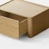 A minimalist wooden box with a single drawer partially open, placed on a light gray surface against a plain white background.