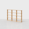 A light wood bookshelf with four horizontal shelves and multiple vertical dividers, standing empty on a gray floor against a plain white background.