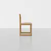 A minimalist wooden chair with a square, geometric design, shown in side profile against a plain white background and light grey floor.