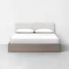 A modern bed with a light wood frame, white headboard, white bedding, and two pillows, set against a plain white wall and floor background.