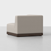 A modern, armless beige upholstered chair with a low back and seat, featuring a dark wooden base, is placed on a light gray floor against a plain white background.