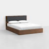 A modern wooden bed frame with a dark upholstered headboard, dressed in white bedding and two pillows, is set against a plain white background.