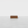 A single rectangular wooden box sits on a smooth, light gray floor against a plain white background.