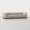 A modern beige sectional sofa with three seats, featuring clean lines and a dark wooden base, set against a plain white background.