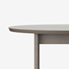 Close-up of the edge and leg of a round wooden table with a smooth, light brown finish against a plain white background.