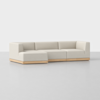 A modern, L-shaped sectional sofa with light beige upholstery and a wooden base, set on a plain light gray floor with a white background.