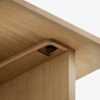 Close-up of a wooden table or shelf corner, showing a metal fastener or screw securing the horizontal and vertical wooden panels together, against a plain white background.
