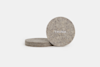 Four round, gray felt coasters stacked on a white surface. The coaster in front stands upright and displays the word THUMA in white uppercase letters.