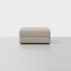 A light beige, rectangular upholstered ottoman with clean lines sits on a smooth, light gray floor against a plain white background.