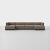 A modern, modular brown sectional sofa with four connected seats and low backs, placed in a minimalist, white room with a light floor.