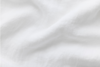 A close-up of soft, white, slightly wrinkled fabric with gentle folds and subtle texture.