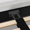 Close-up of a bed frame showing a black metal support bracket attached to light wooden slats and secured to the upholstered bed base with screws. A black fabric strap is also visible across the slats.