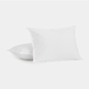 Two plain white pillows with smooth fabric covers are placed on a white surface, with one pillow standing upright and the other laying flat behind it.